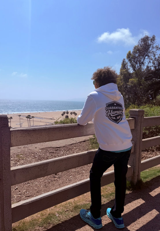 Michel, 5'8" — A windy day in Santa Monica, CA in the Guaranteed Human™ Men Crest + Back Hoodie, size S.